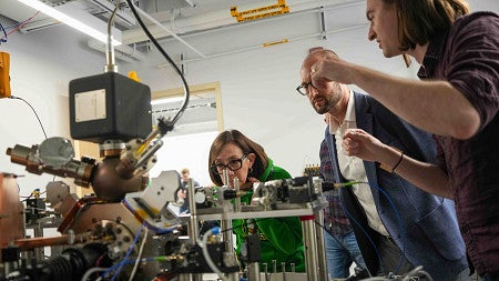 Congresswoman Andrea Salinas leans in to examine quantum research instrumentation as UO faculty explain the setup inside a campus laboratory.